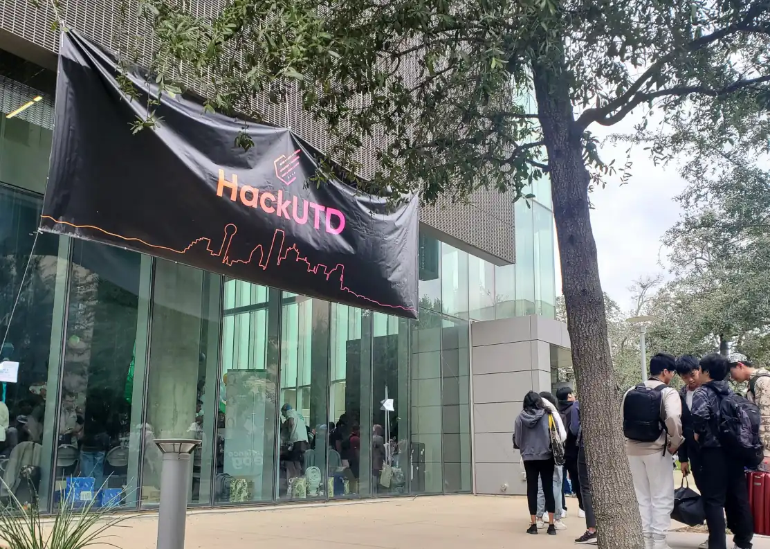 glass-walled university building with large HackUTD banner suspended over vestibule