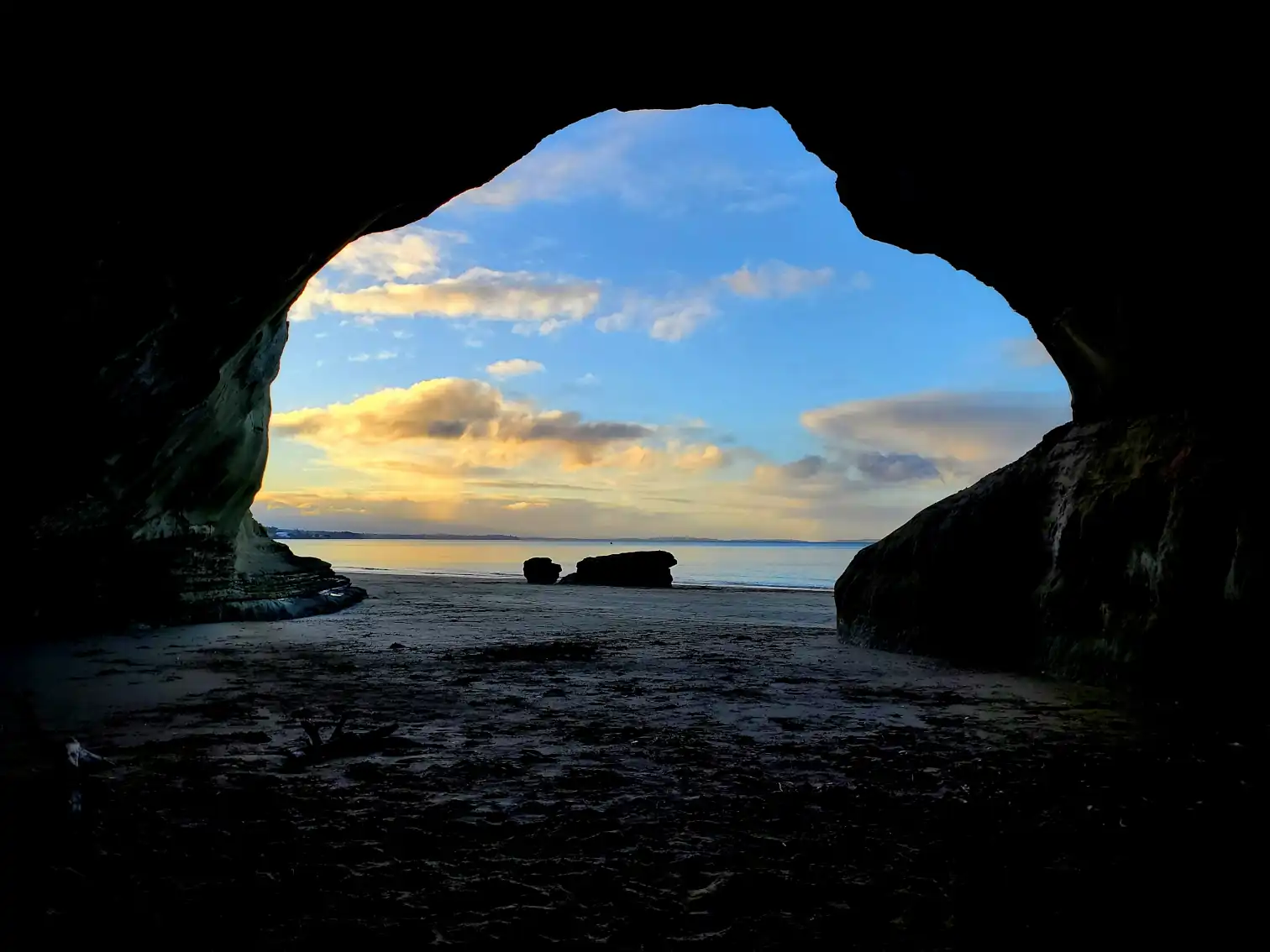 sunset over the ocean seen from inside a cave on Takapuna Beach