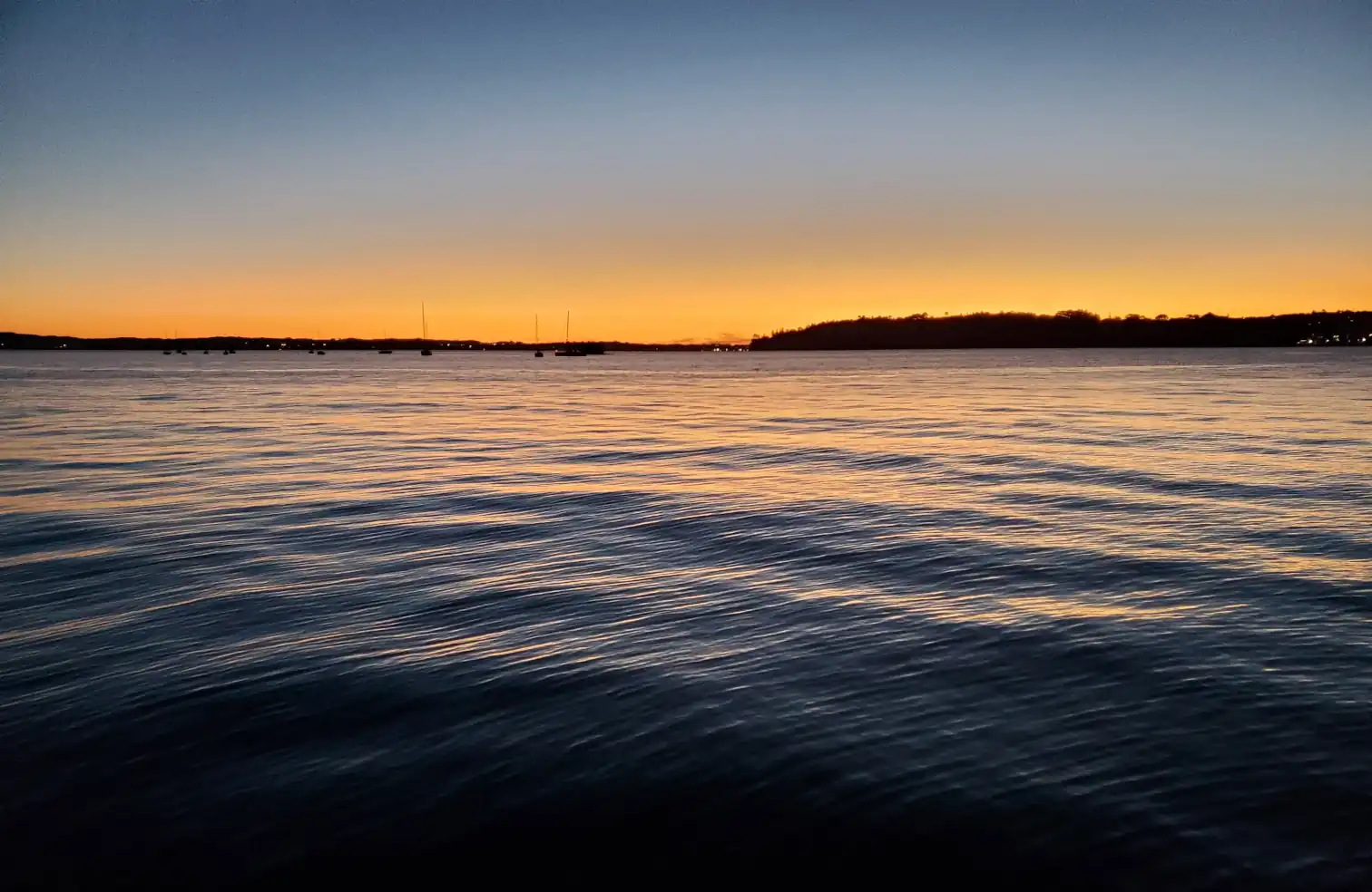 sunset reflecting in calm waters with a few boats